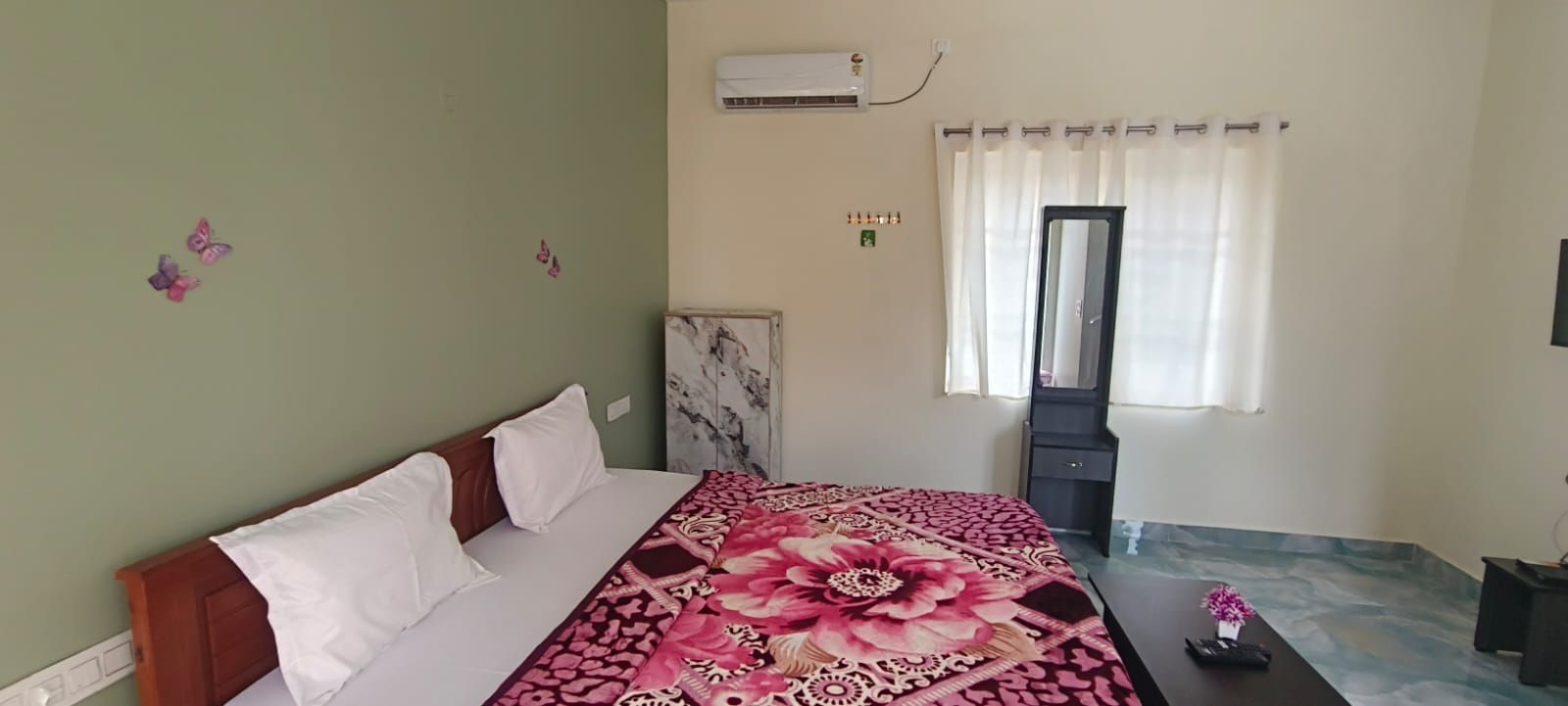 Un dormitorio con cama, mesita de noche, espejo y ventana con cortinas.