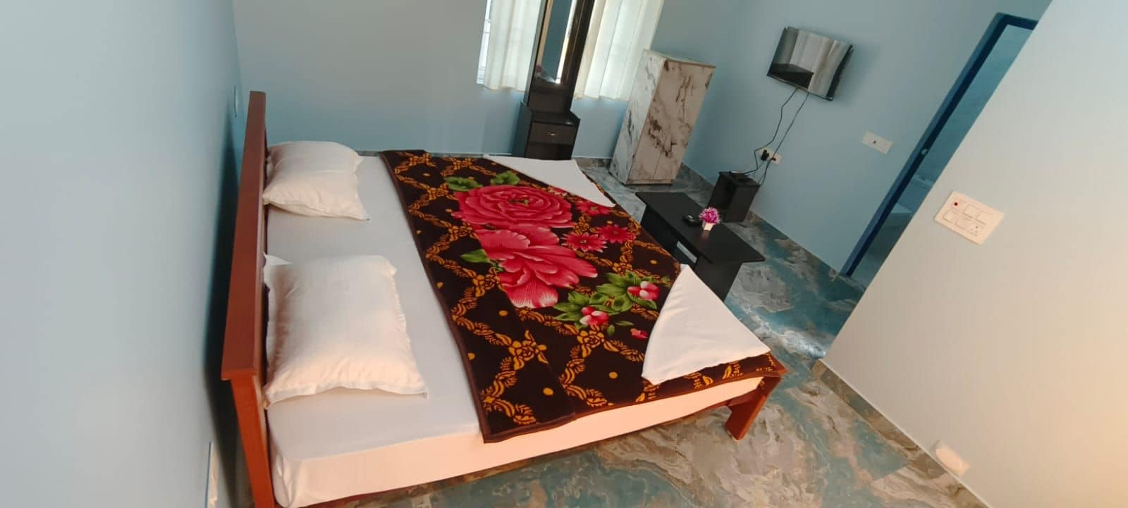 Un dormitorio con cama, almohadas, una colcha decorativa, una mesita de noche, un aparador y un televisor.