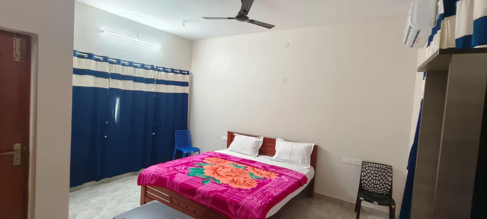 Une chambre à coucher avec un lit, une chaise, un ventilateur de plafond et un rideau.