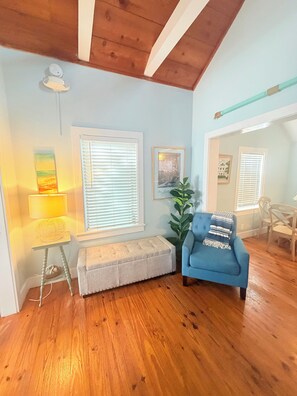 A room with wooden flooring, a blue armchair, a bench, a lamp, and a plant. - TIDES ON SIMONTON - 1 Bedroom / 1 Bathroom Steps from Duval Street (Key West)