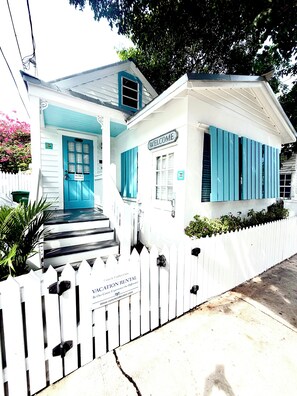 A white building with blue shutters and a 'Welcome' sign, a white picket fence, and a 'Vacation Rental' sign. - TIDES ON SIMONTON - 1 Bedroom / 1 Bathroom Steps from Duval Street (Key West)