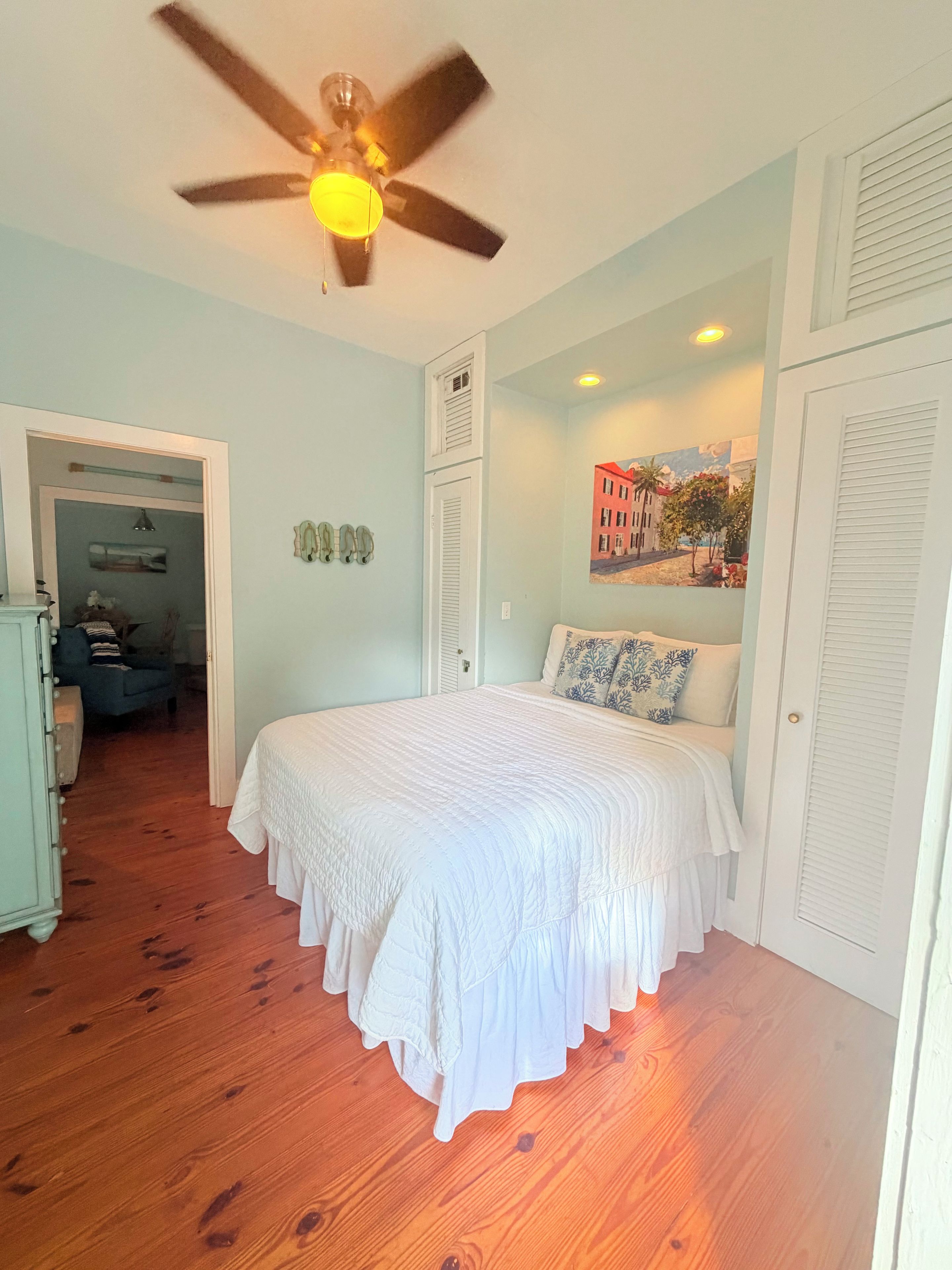 Une chambre à coucher avec un lit, un ventilateur de plafond, un tableau et une porte.