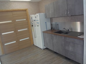 Eine Küche mit grauen Schränken, einer Holzarbeitsplatte, einem Spülbecken und einem weißen Kühlschrank.