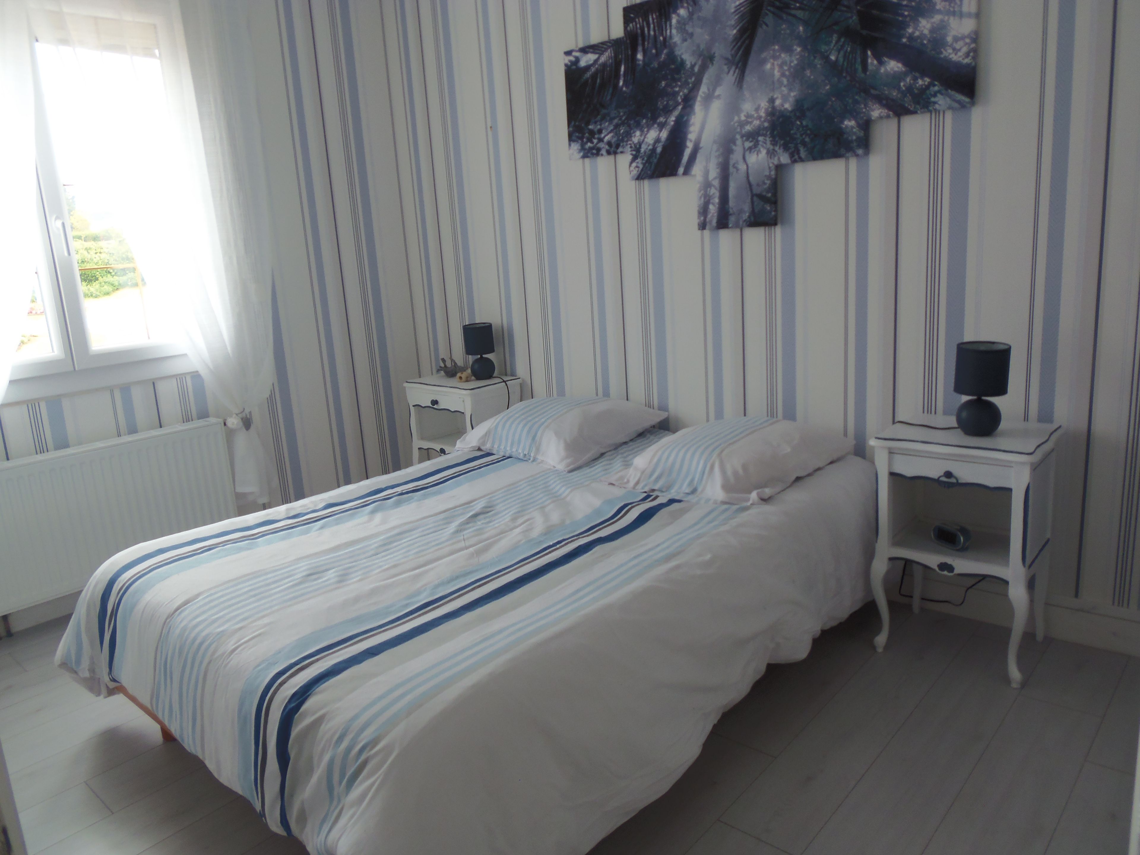 A bedroom with a bed, two bedside tables, a radiator, and a window.