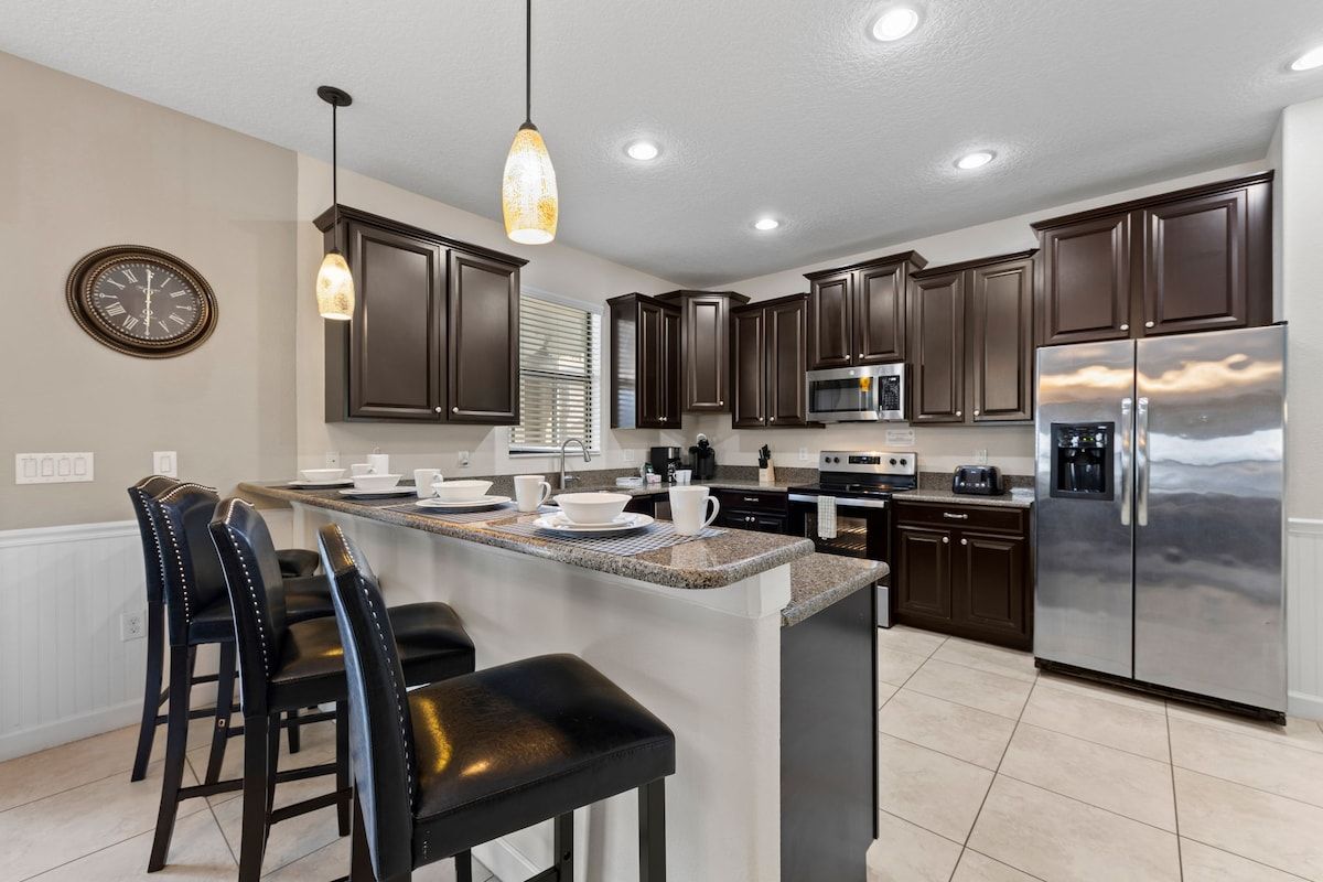 A modern kitchen with dark cabinetry, stainless steel appliances, and a central island with bar stools.