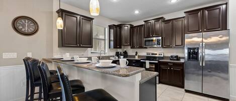A modern kitchen with dark cabinetry, stainless steel appliances, and a central island with bar stools.