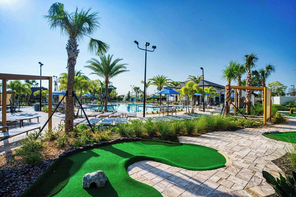 A pool area with palm trees, lounge chairs, and a small putting green.