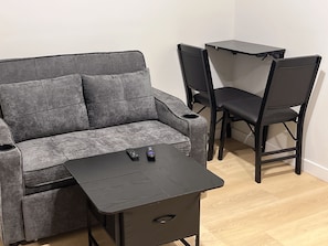 Ein graues Sofa, ein kleiner Tisch und zwei Stühle in einem Zimmer mit Holzboden.