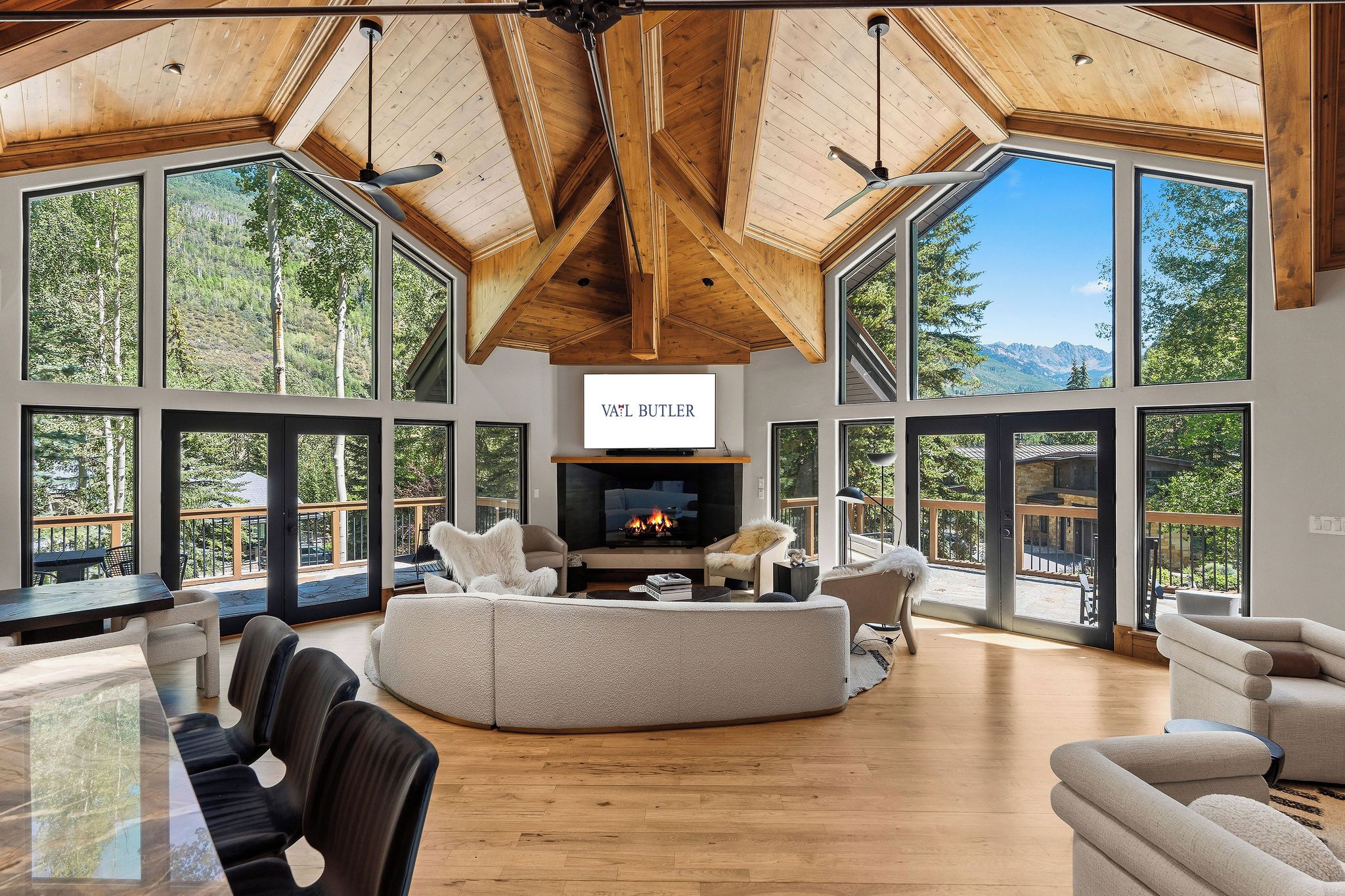 A spacious living room with a fireplace, large windows, and a high ceiling with wooden beams.