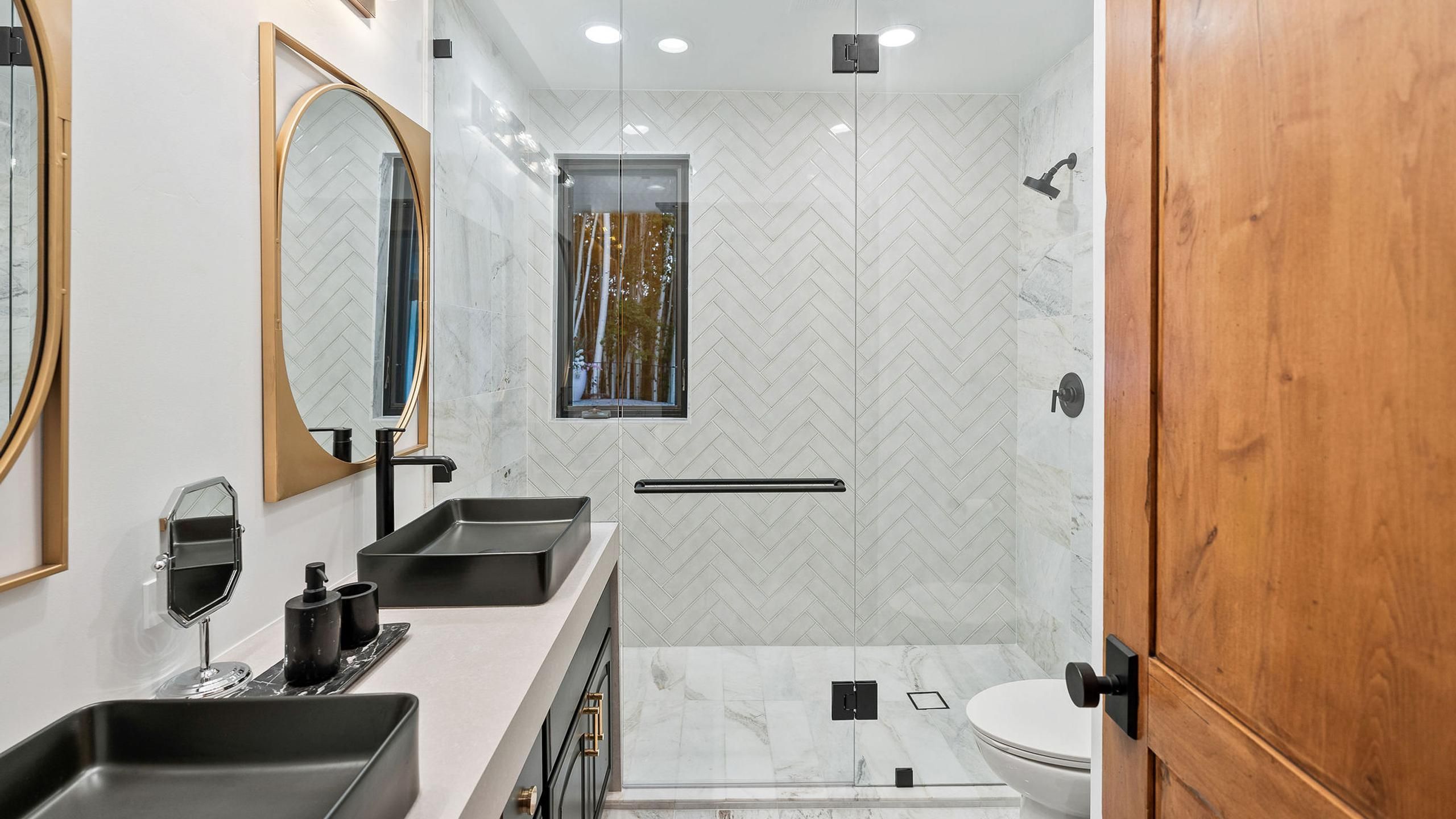 Un baño moderno con un espejo grande, dos lavamanos, un inodoro y una zona de ducha.