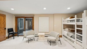 Una habitación con puerta de madera, ventana, una cama litera blanca y dos sillas.