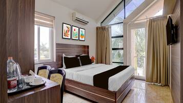 A hotel room with a bed, a desk with a chair, a flat-screen TV, and a window with curtains.