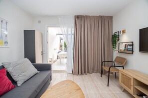 Ein modernes Wohnzimmer mit einem grauen Sofa, einem Holztisch, einem Korbstuhl, einem Holzschrank und einem großen Fenster mit Vorhängen.