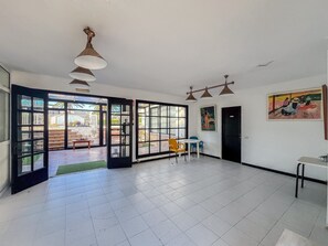 Ein geräumiges Zimmer mit einem großen Schiebeglasfenster, das zu einem Außenbereich führt, einem kleinen Tisch mit Stühlen und einem Bild an der Wand.