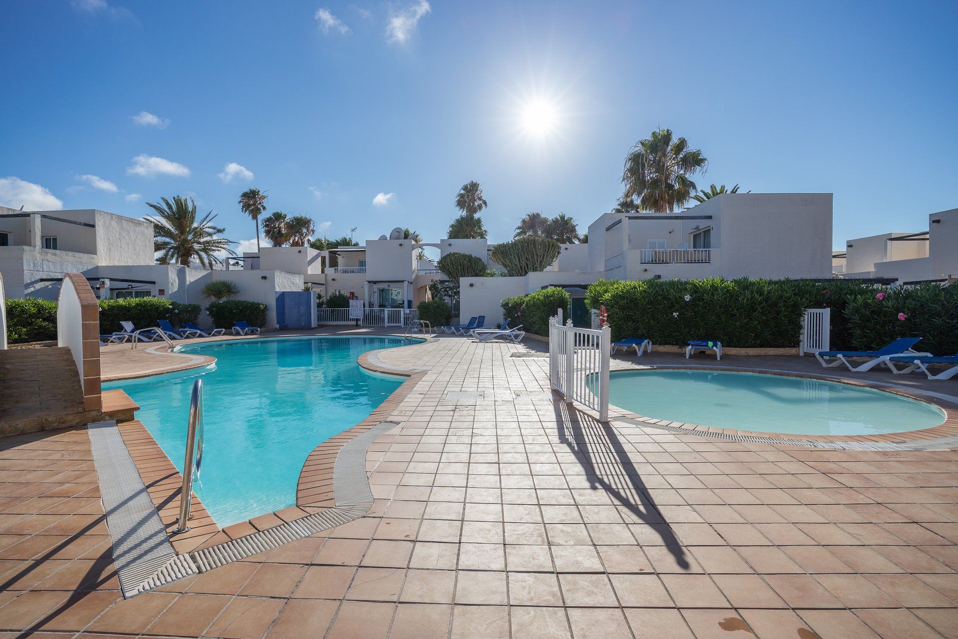A swimming pool area with two pools, sun loungers, and a clear sky.