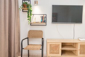 A room with a chair, a wooden console table, a wall-mounted TV, and a shelf with books and a plant. - GuestReady - Los Alisios Corralejo 39 (La Oliva)