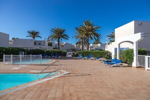 A pool area with a tiled deck, lounge chairs, and palm trees. - GuestReady - Los Alisios Corralejo 39 (La Oliva)