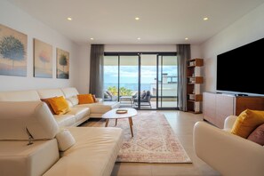 A modern living room with a sofa, coffee table, and a flat-screen TV. There are large windows with a view of the sea. - LME81B - Sea view terrace - indoor pool (Estepona)