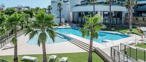 A modern hotel with a swimming pool, palm trees, and a view of the city.