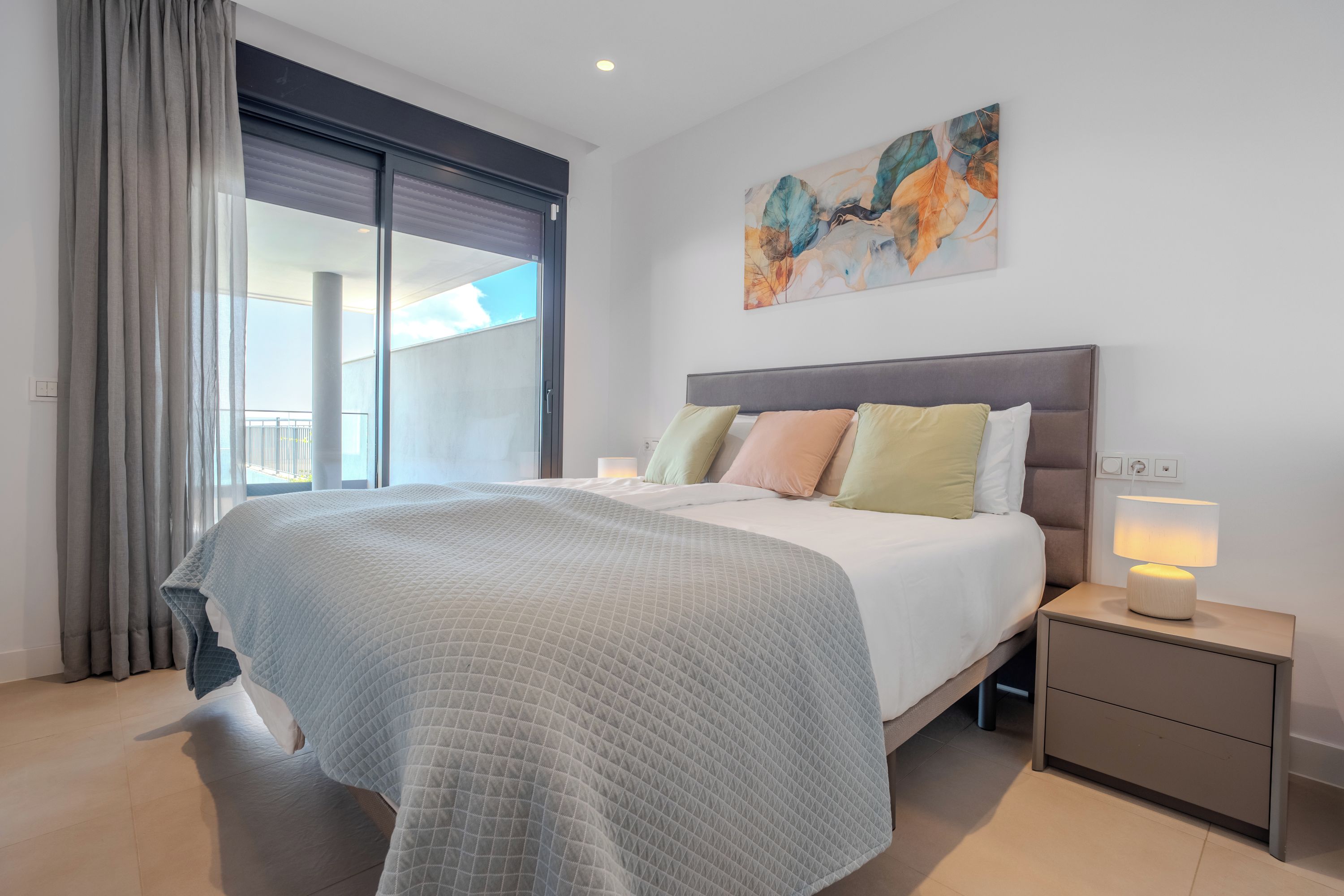 Une chambre à coucher moderne avec un grand lit, une table de chevet, une lampe et un tableau au mur.