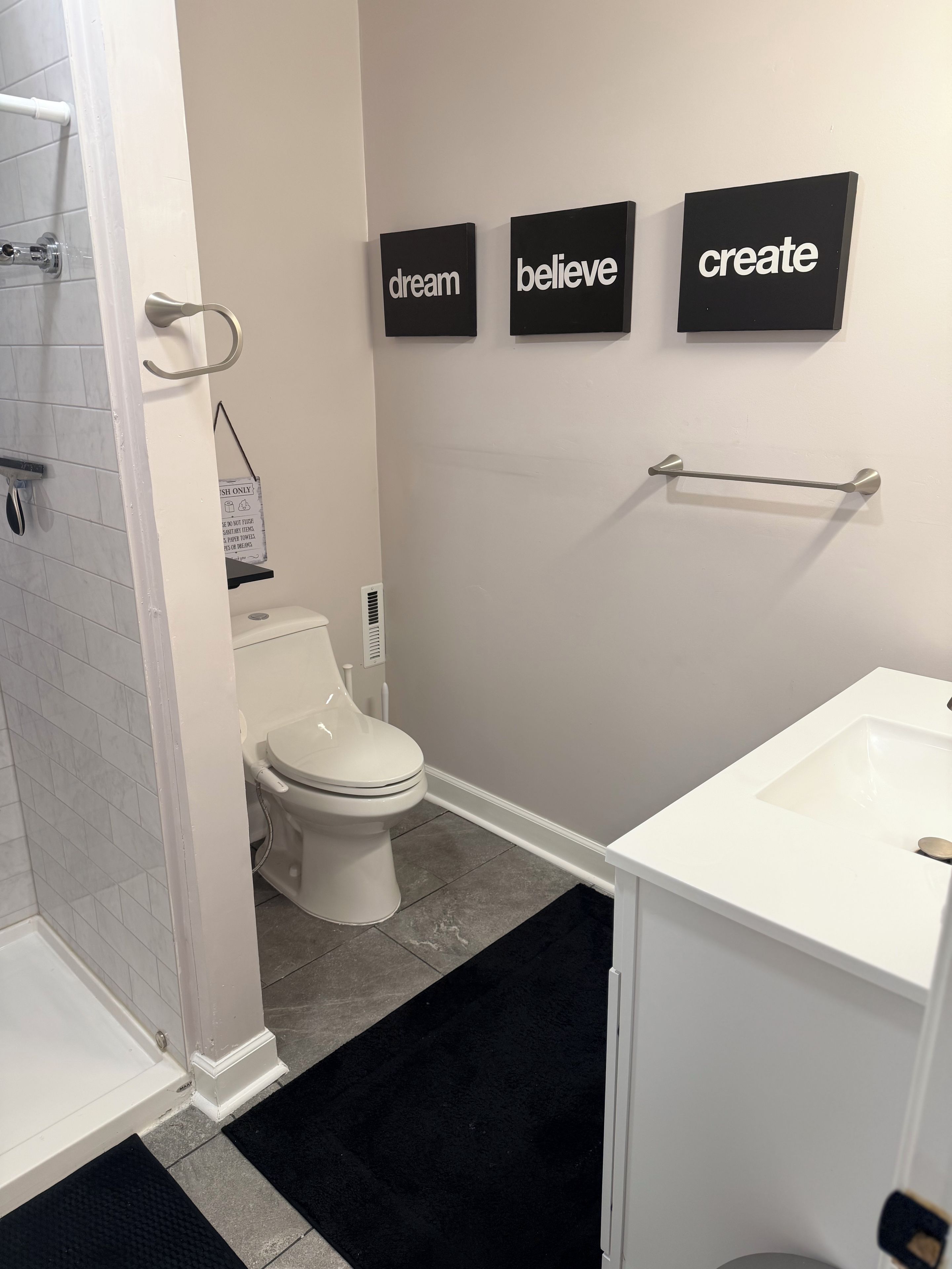 A bathroom with a toilet, a sink, and a shower area. There are motivational words on the wall.