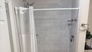 A shower area with a white curtain, a showerhead, and a tiled wall. - Private Studio Suite in Woodbridge, VA Near I-95 & VRE (Woodbridge)