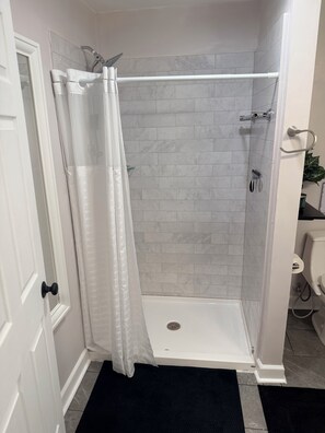 A shower area with a white curtain, a showerhead, and a tiled wall. - Private Studio Suite in Woodbridge, VA Near I-95 & VRE (Woodbridge)