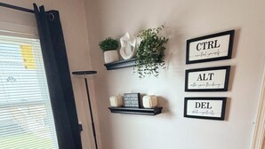 A dark-colored sofa with a white pillow, a small shelf with decorative items and framed motivational quotes, and a floor lamp. - Private Studio Suite in Woodbridge, VA Near I-95 & VRE (Woodbridge)