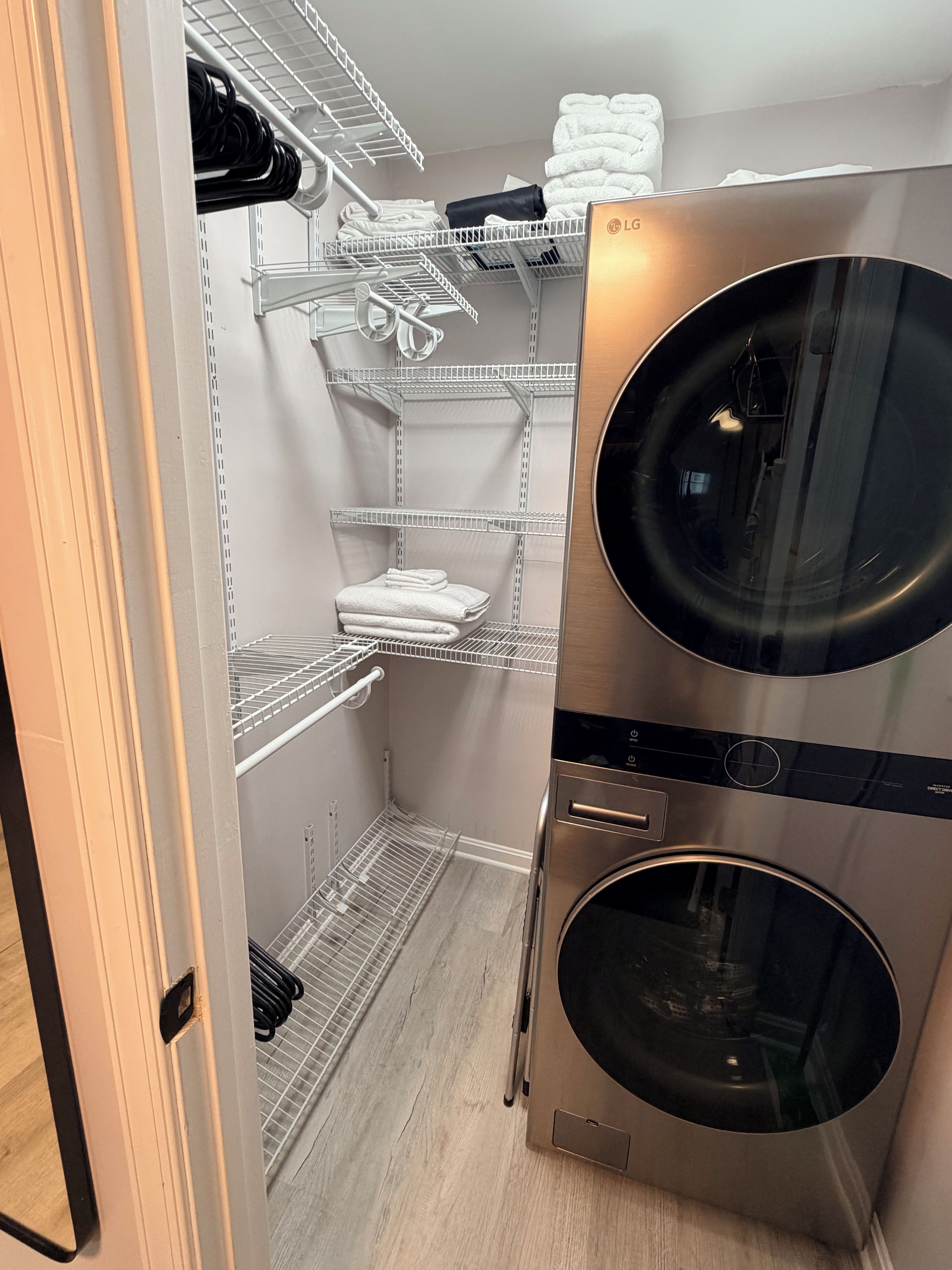 A laundry room with a front-loading washing machine, metal shelves for towels, and a door leading to another room.