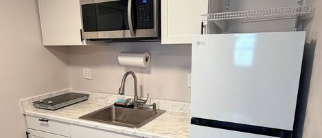 A modern kitchen with white cabinets, a stainless steel sink, a microwave, and a refrigerator.