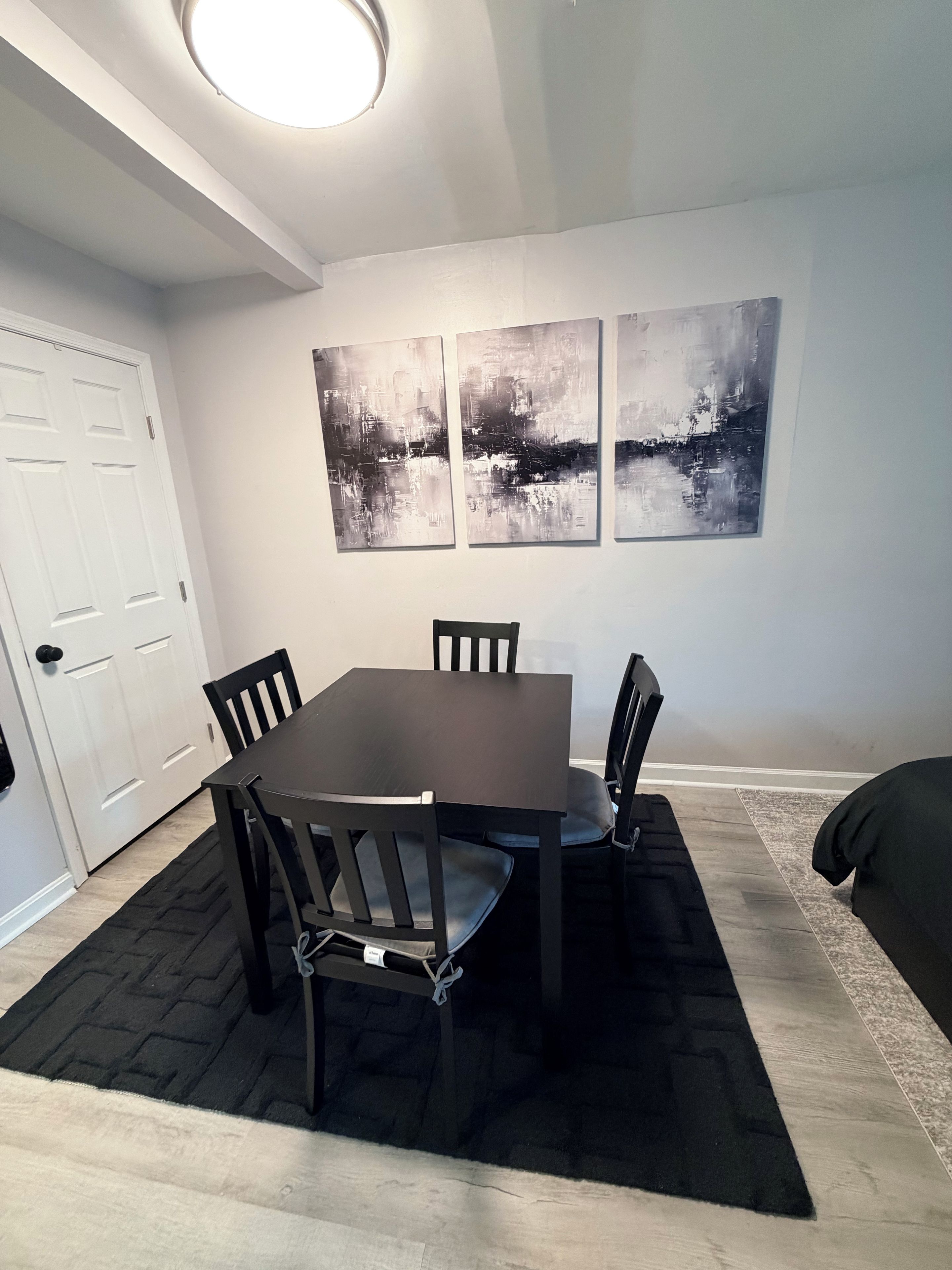 A dining area with a table and chairs, a black rug, and abstract wall art.
