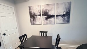 A dining area with a table and chairs, a black rug, and abstract wall art. - Private Studio Suite in Woodbridge, VA Near I-95 & VRE (Woodbridge)