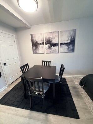 A dining area with a table and chairs, a black rug, and abstract wall art. - Private Studio Suite in Woodbridge, VA Near I-95 & VRE (Woodbridge)
