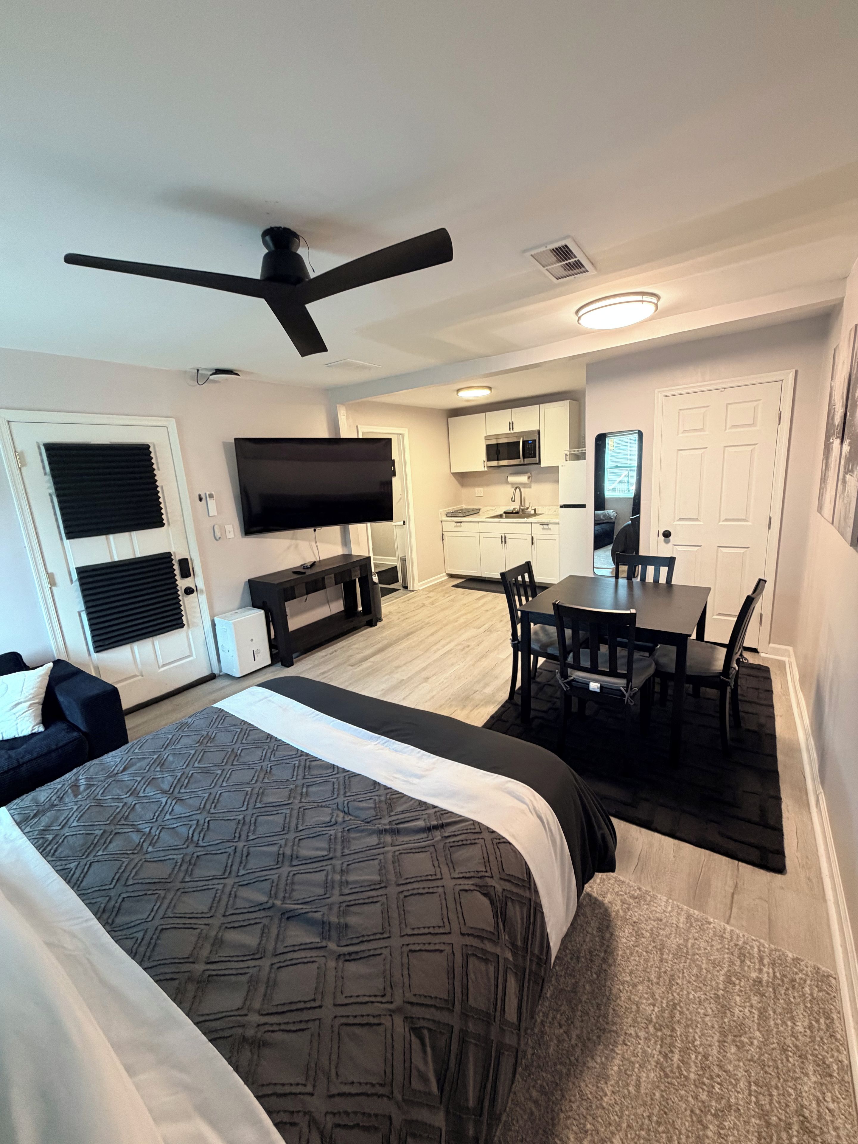 A compact hotel room with a bed, a desk, a chair, a television, and a kitchenette.