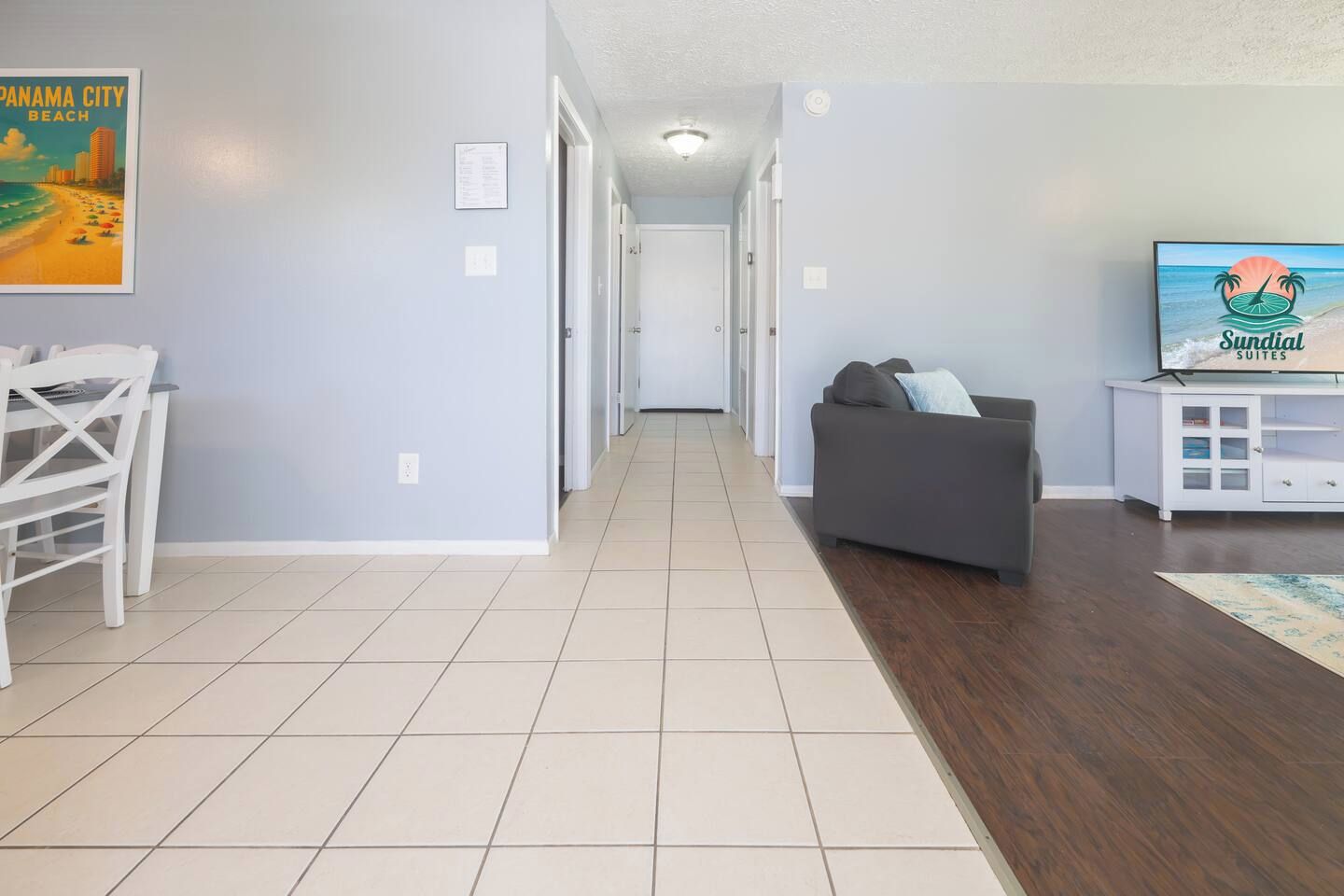 A hallway with a dining area, a sofa, and a television displaying 'Sundial Suites'.