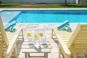 Zona piscina con poltrone relax, un tavolo con bevande e vista diretta sulla piscina.