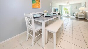 A dining area with a table set for four, white chairs, and a bench. - 1/2 Block to the Beach, West End | Balcony+Pool (Panama City Beach)