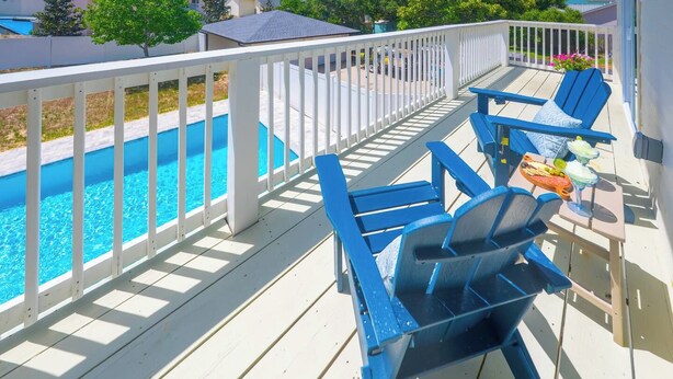 A deck with a pool, blue chairs, and a table with drinks. - 1/2 Block to the Beach, West End | Balcony+Pool (Panama City Beach)
