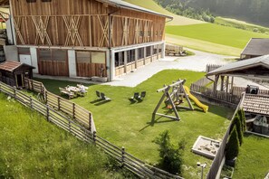 A barn with a covered outdoor area, a fenced play area with benches, and a small building to the left.