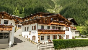 Un edificio de estilo chalete tradicional con varios balcones, fachada de piedra y vistas a una montaña boscosa.
