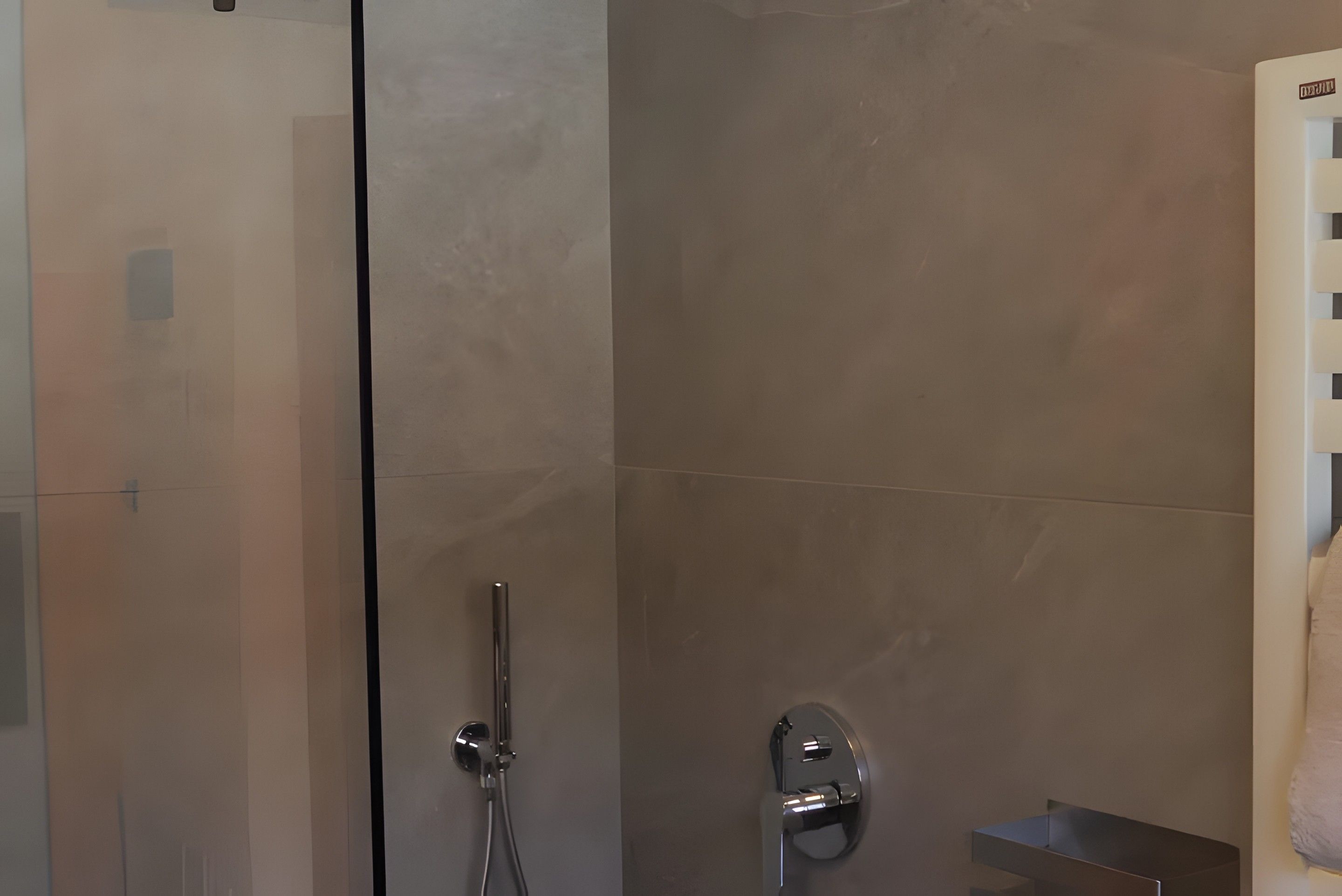 Une salle de bain moderne dotée d’une douche à parois de verre, d’un pommeau de douche à main et d’un robinet mural.