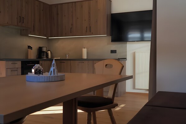 A modern kitchen with wooden cabinets, a flat-screen TV, and a dining area with a table and chairs.