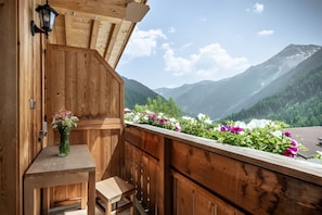 A wooden balcony with a table and chair, overlooking a mountainous landscape.
