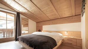 Un dormitorio con techo de madera, una cama con cabecera oscura, una mesita de noche y una ventana con cortinas.