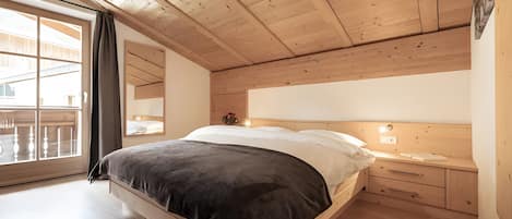 A bedroom with a wooden ceiling, a bed with a dark headboard, a nightstand, and a window with curtains.