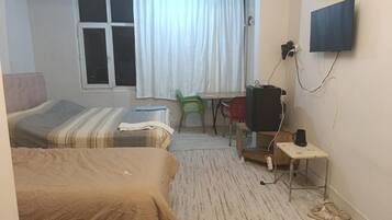 Habitación de hotel con dos camas, televisión, escritorio y ventana con cortinas.