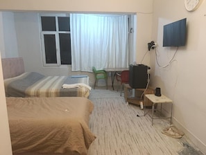 Quarto de hotel com duas camas, televisão, escrivaninha e janela com cortinas.