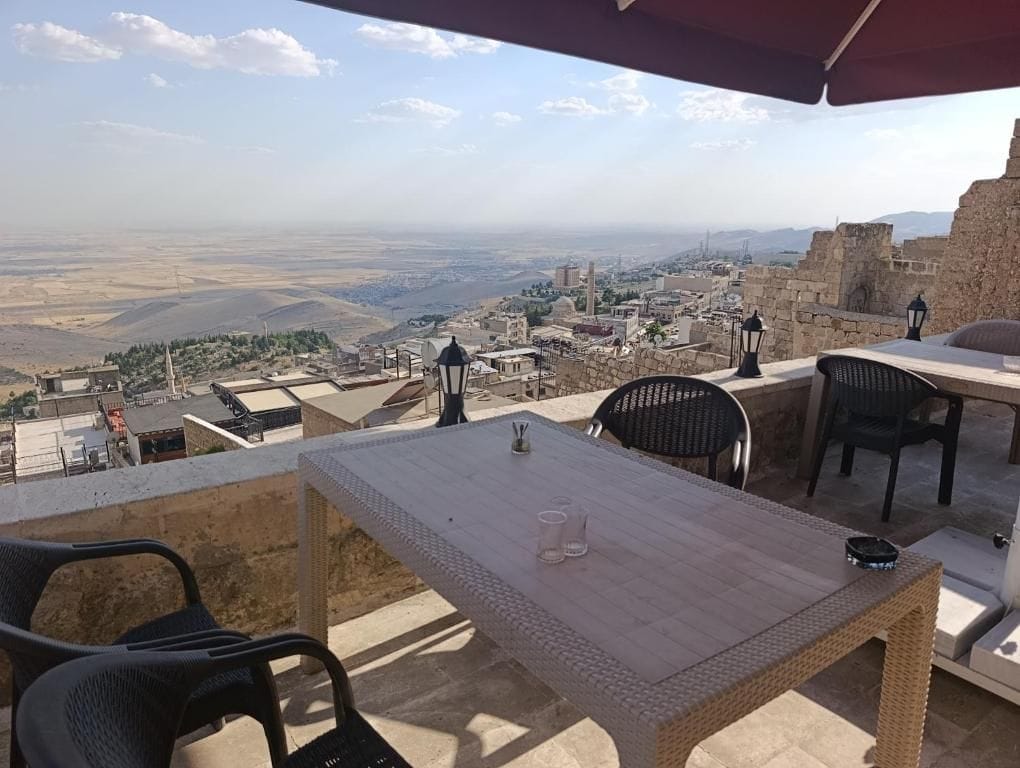An outdoor terrace with a table and chairs, overlooking a cityscape with historical buildings and a distant view of the countryside.