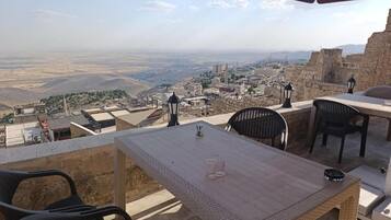 An outdoor terrace with a table and chairs, overlooking a cityscape with historical buildings and a distant view of the countryside.