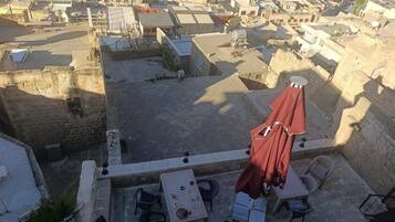 A rooftop terrace with tables and chairs, a red umbrella, and a view of a cityscape.